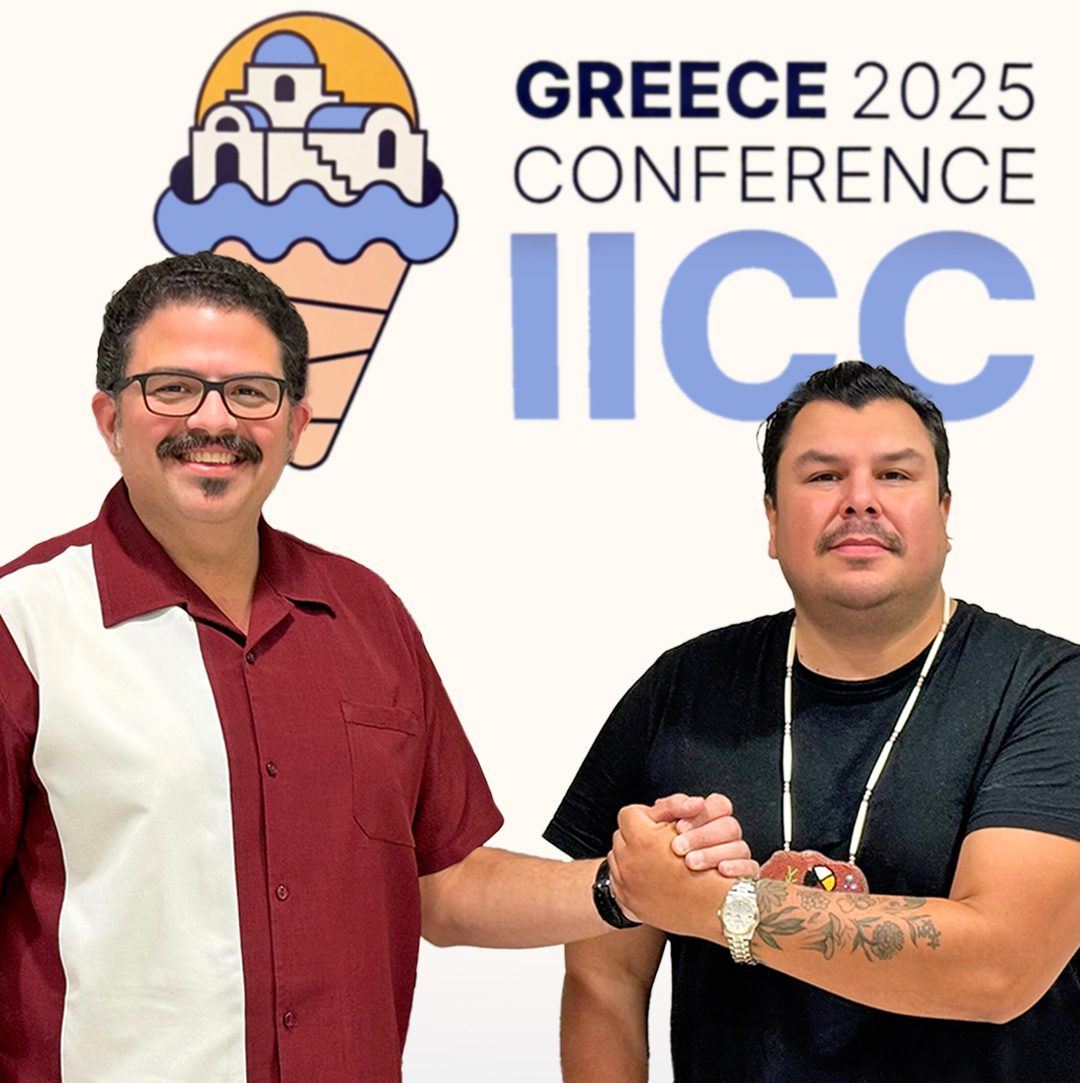 Ashley Chapman and Zach Keeshig lock hands in collaboration as they stand in front of a sign with the IICC Greece conference logo. Ashley Chapman et Zach Keeshig s’empoignent la main en signe de collaboration devant une affiche montrant le logo du congrès de l’IICC en Grèce.