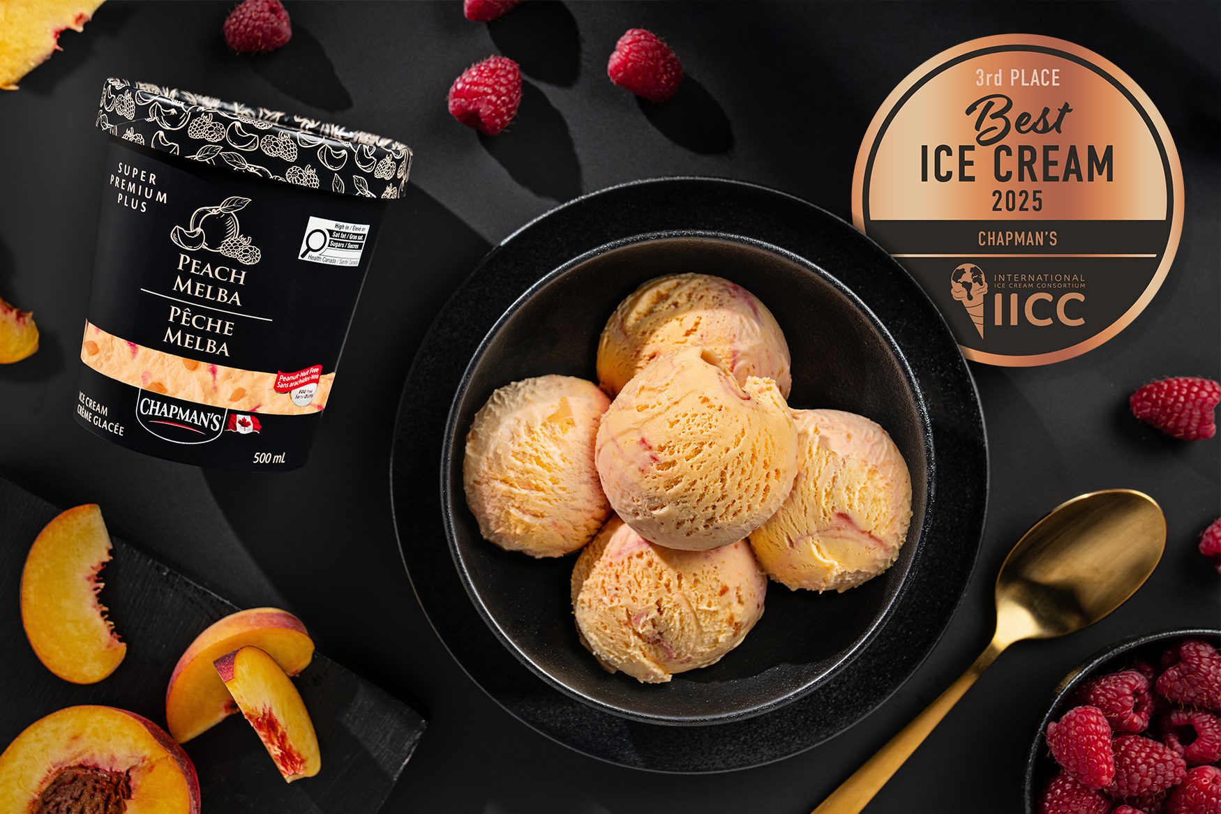 An overhead view of a black bowl full of scoops of Chapman’s Super Premium Plus Peach Melba ice cream. Beside the bowl is a tub of Peach Melba ice cream.