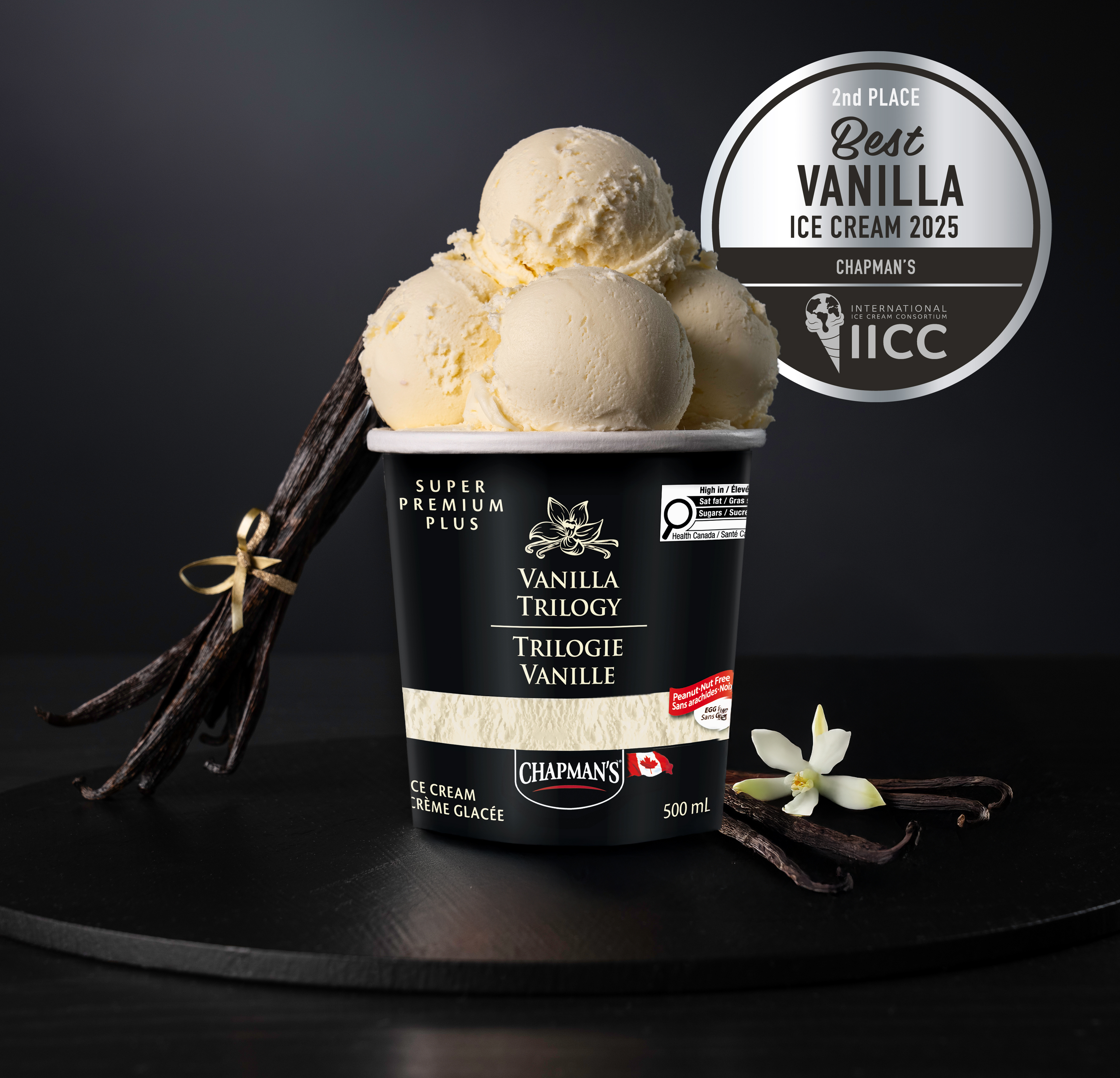 Standing out from a luscious black background is a container of Chapman’s Vanilla Trilogy ice cream with four large scoops of ice cream on top.