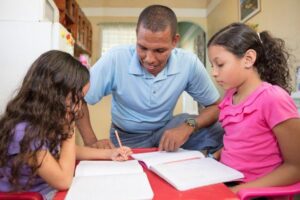 a dad and his two young daughters sitting at a table doing school work